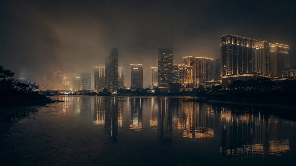 The Cotai Strip in Macau at night, dense resort towers reflected in water with humid air softening the lights