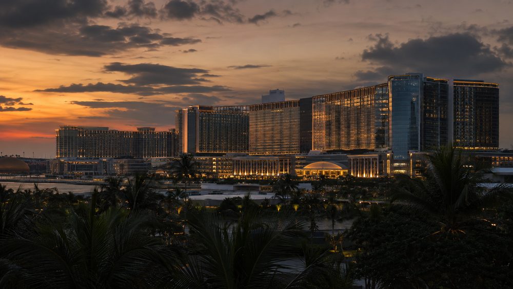 Entertainment City in Manila at dusk, wide integrated-resort architecture against a tropical sky with palm silhouettes in the foreground