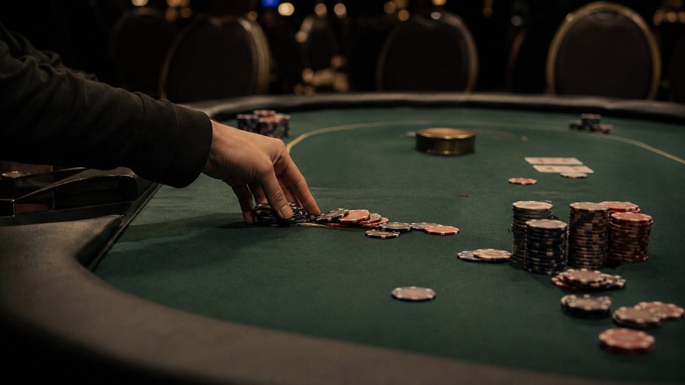 A tournament poker table late in a session, uneven chip stacks and a single hand pushing chips forward